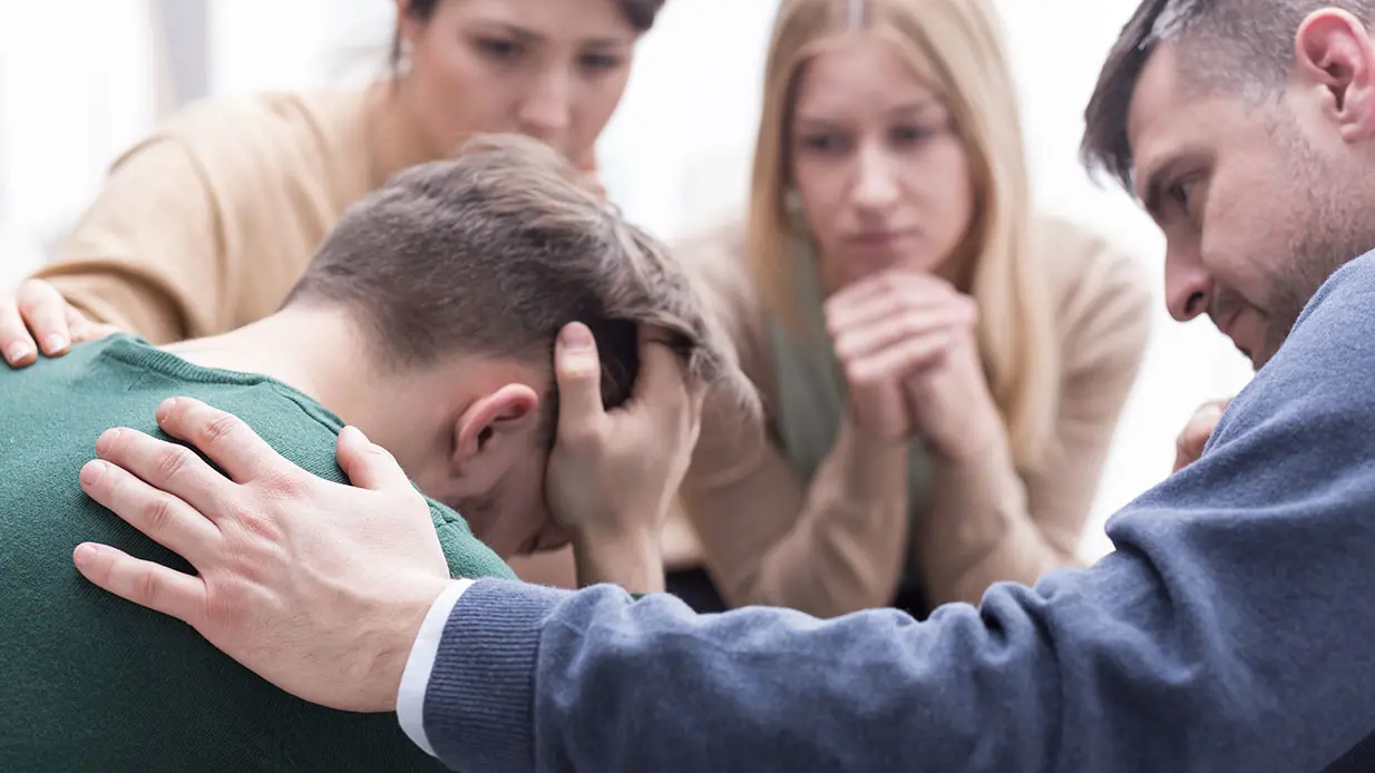 A group of people trying to console a man with his head in his hands. 