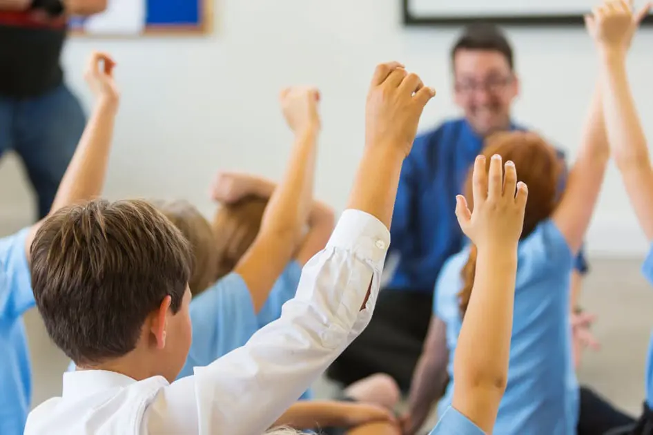 Class of young children raising their hand