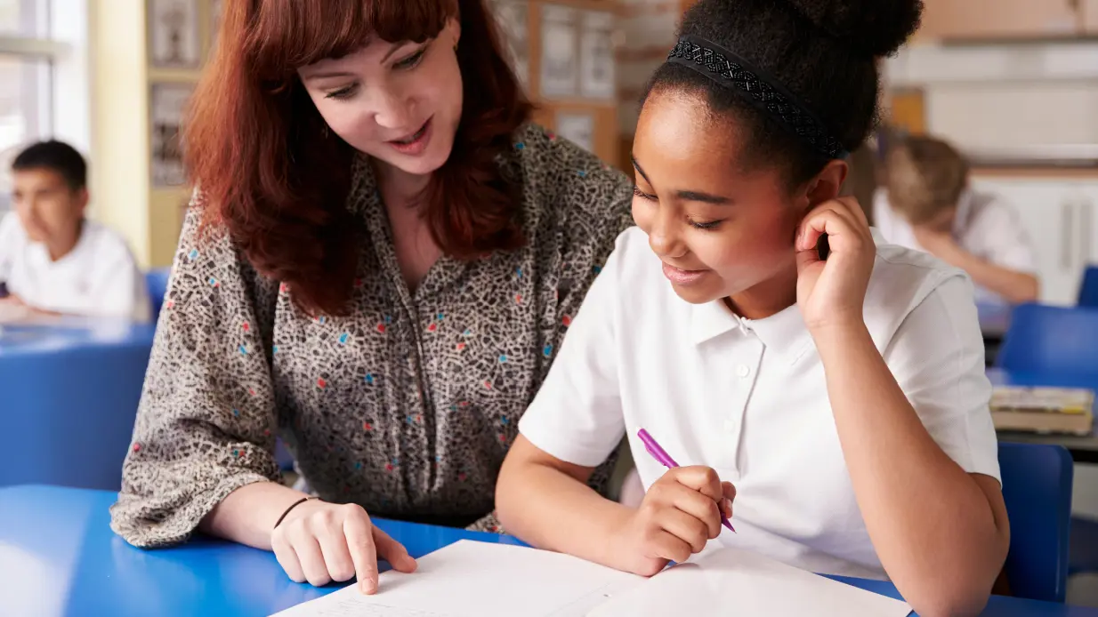 A woman assists a young girl with her homework at a table, fostering a supportive learning environment.