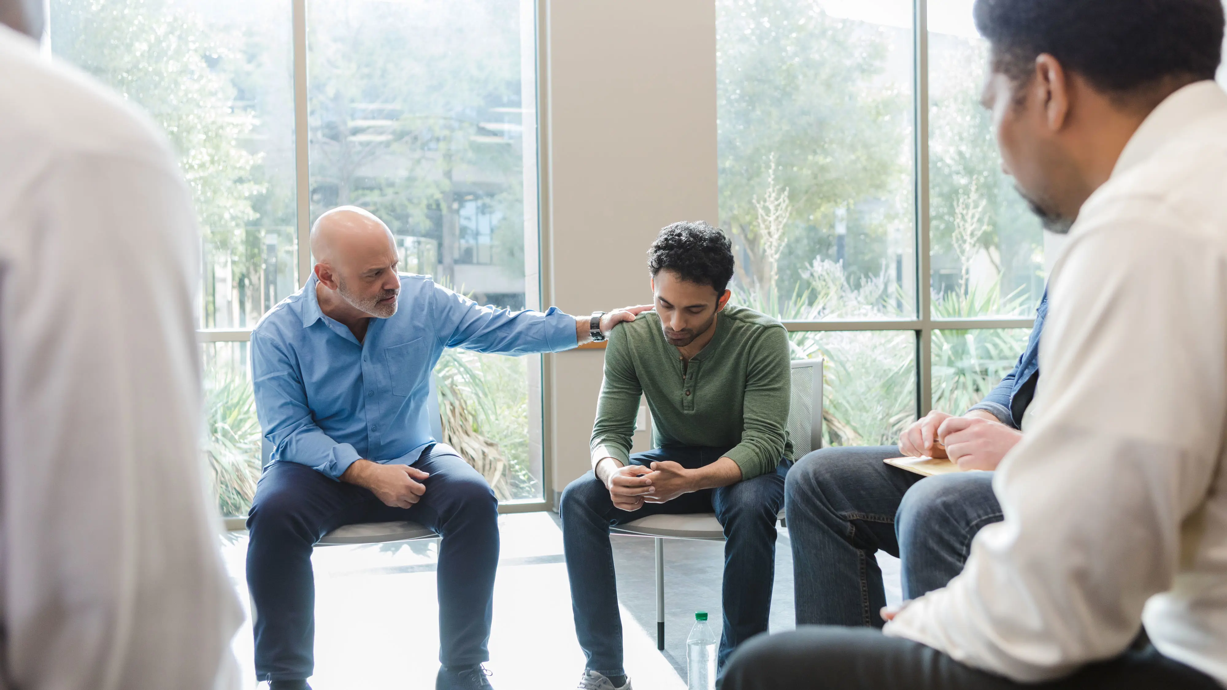 A man with his hand on a shoulder of another man within a group session