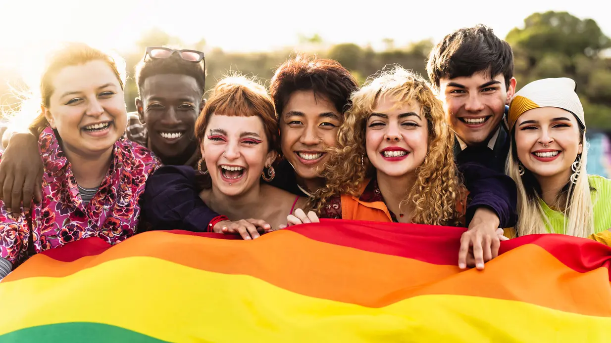 A diverse group of young individuals proudly holding a vibrant rainbow flag, symbolizing unity and support for LGBTQ+ rights.
