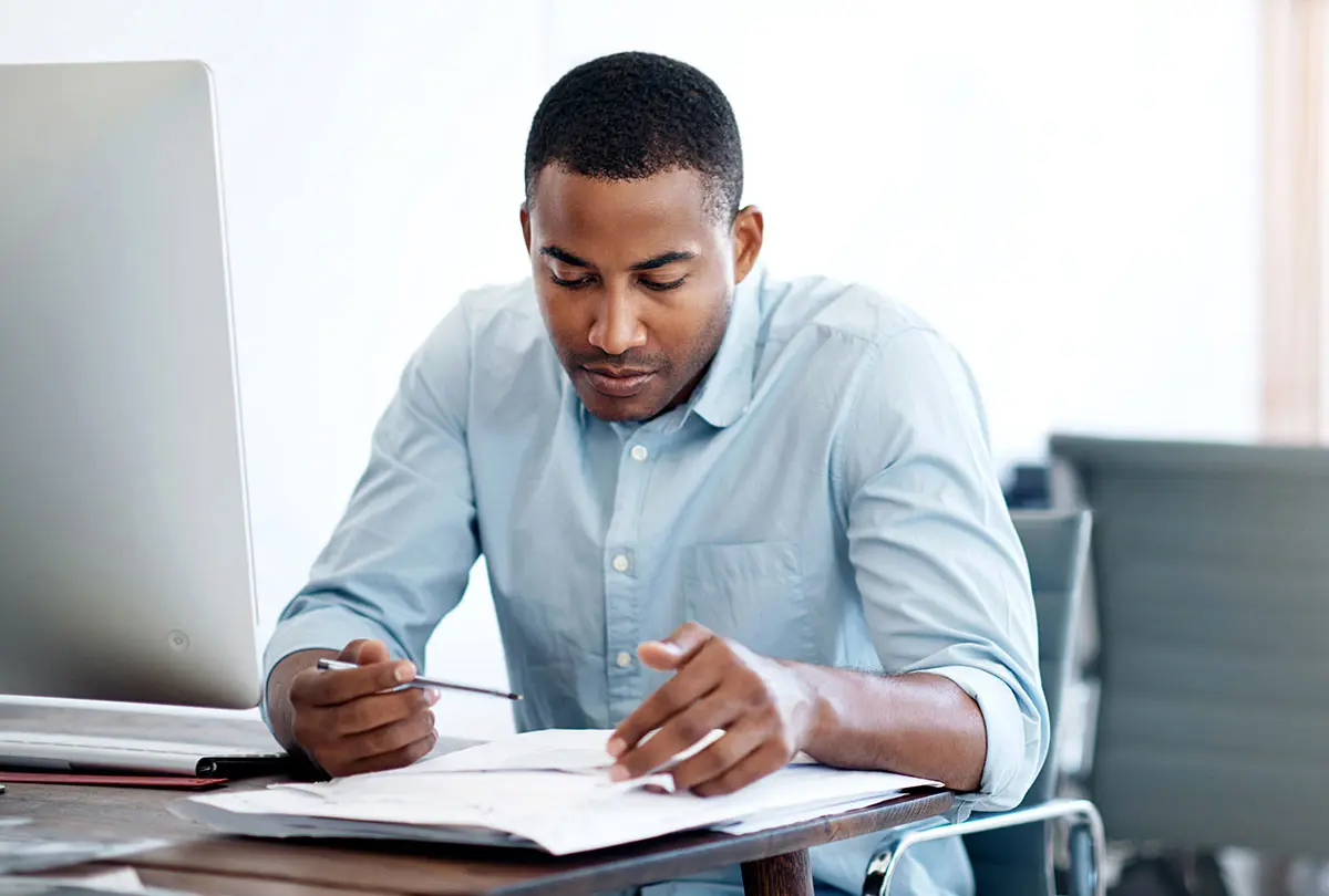 A man at a desk writes with a pen on paper, concentrating on his work.