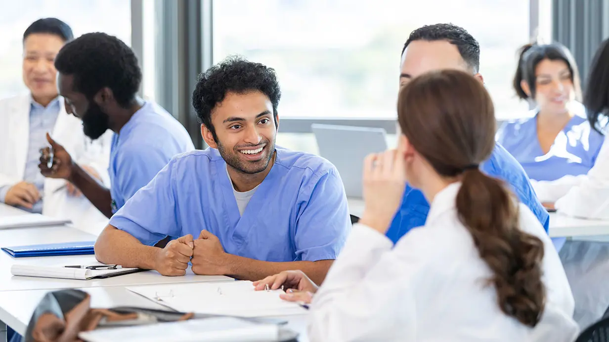 A group of doctors in scrubs engaged in discussion while seated around a table in a professional setting.