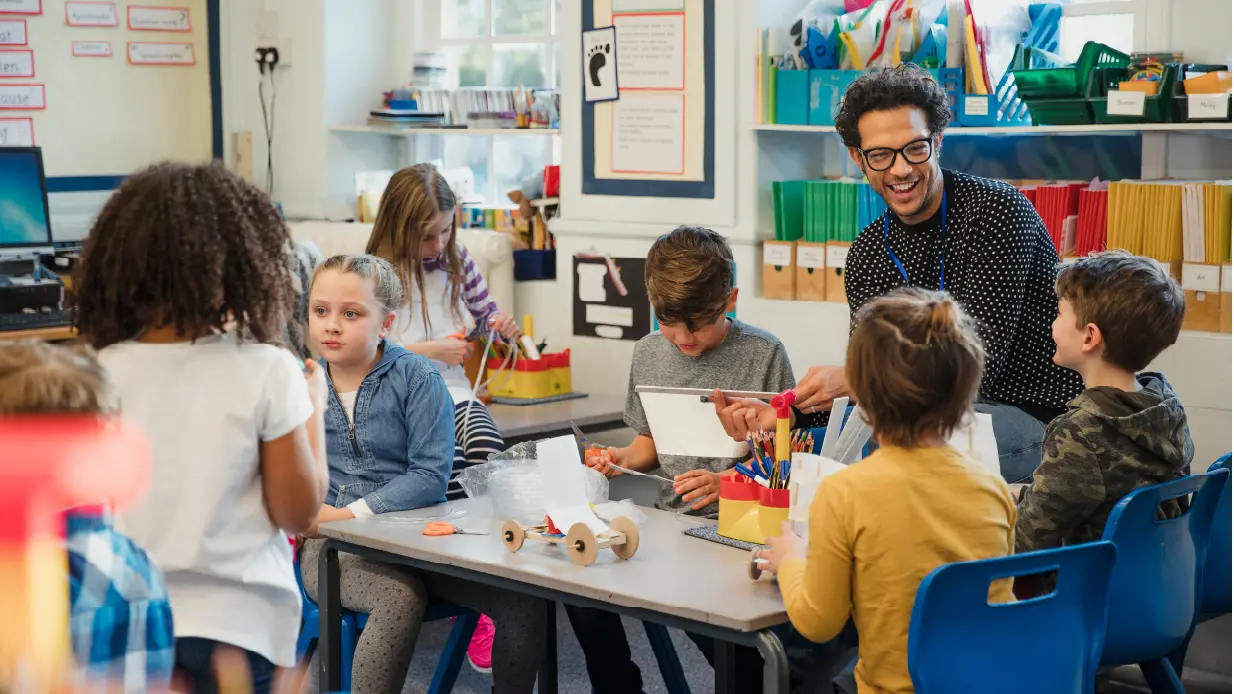 A teacher instructs a group of attentive children in a bright classroom filled with educational materials.