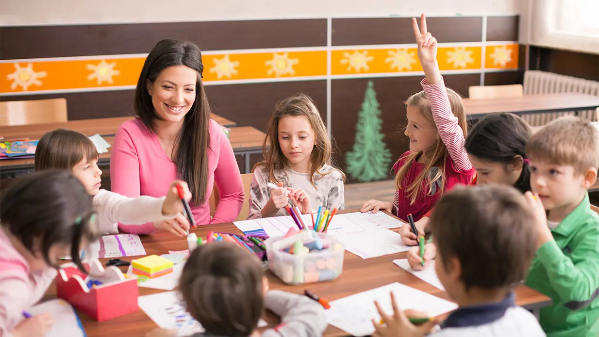 A teacher instructs a group of children gathered around a table, engaged in a learning activity together.