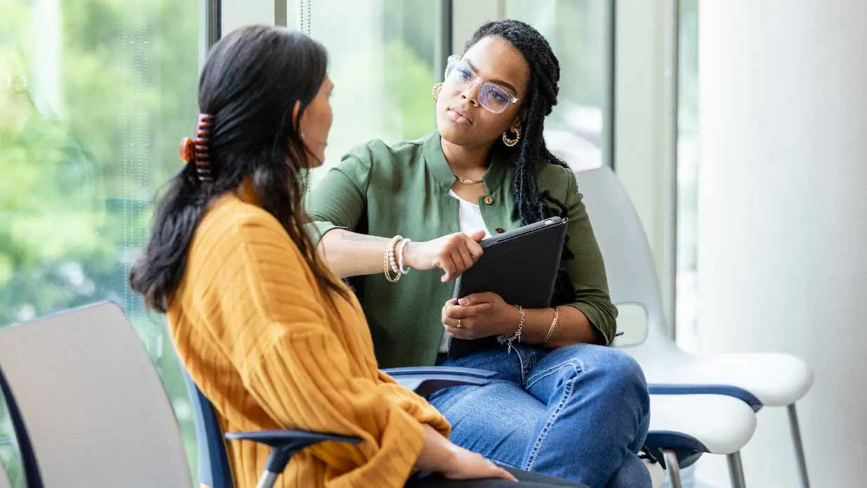 A therapist sits next to a patient and writes notes in a notebook.
