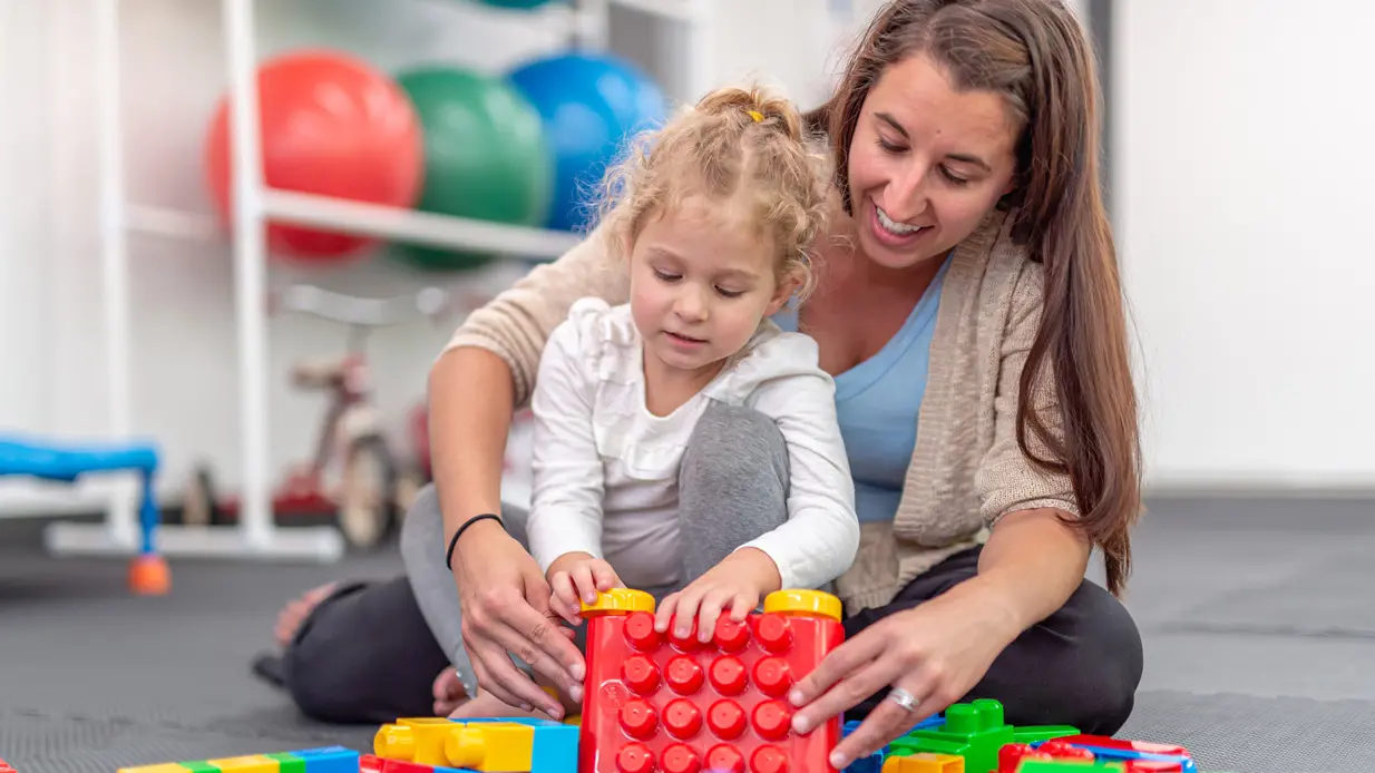 A woman and a child are joyfully playing with colorful blocks on the floor, fostering creativity and bonding.