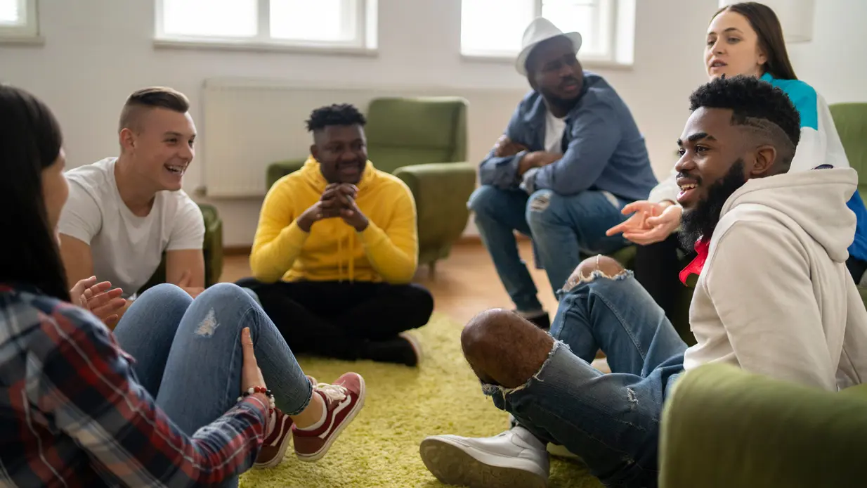 A group of young people gathered in a circle on the floor, participating in a discussion or group activity together.