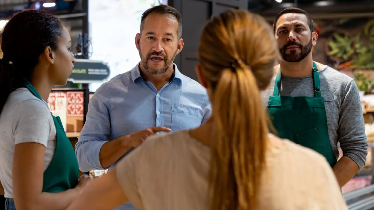 A man and woman discuss with another pair in a grocery store, highlighting a social interaction amidst shopping.