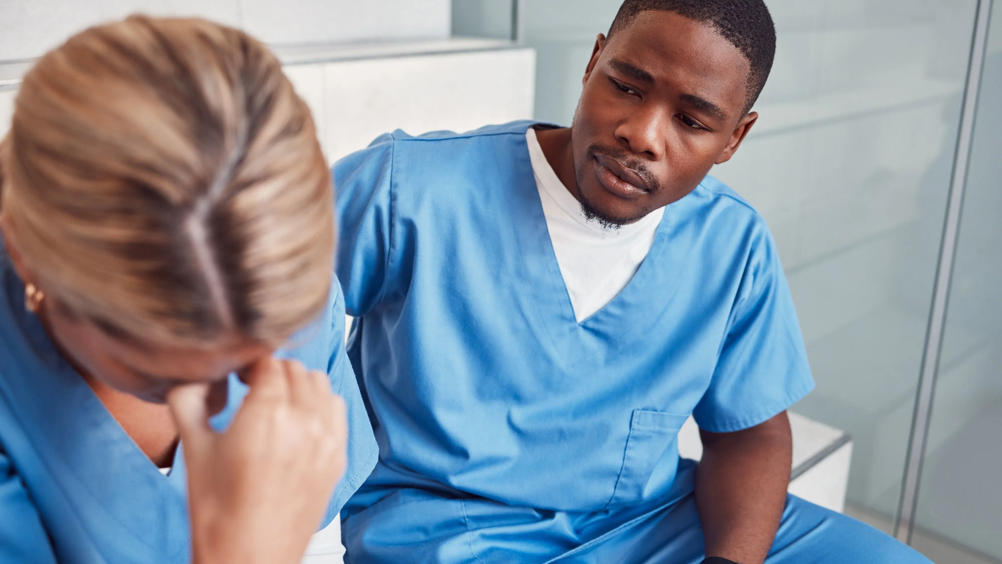 A medical staff member supporting their colleague who has their hand to their head