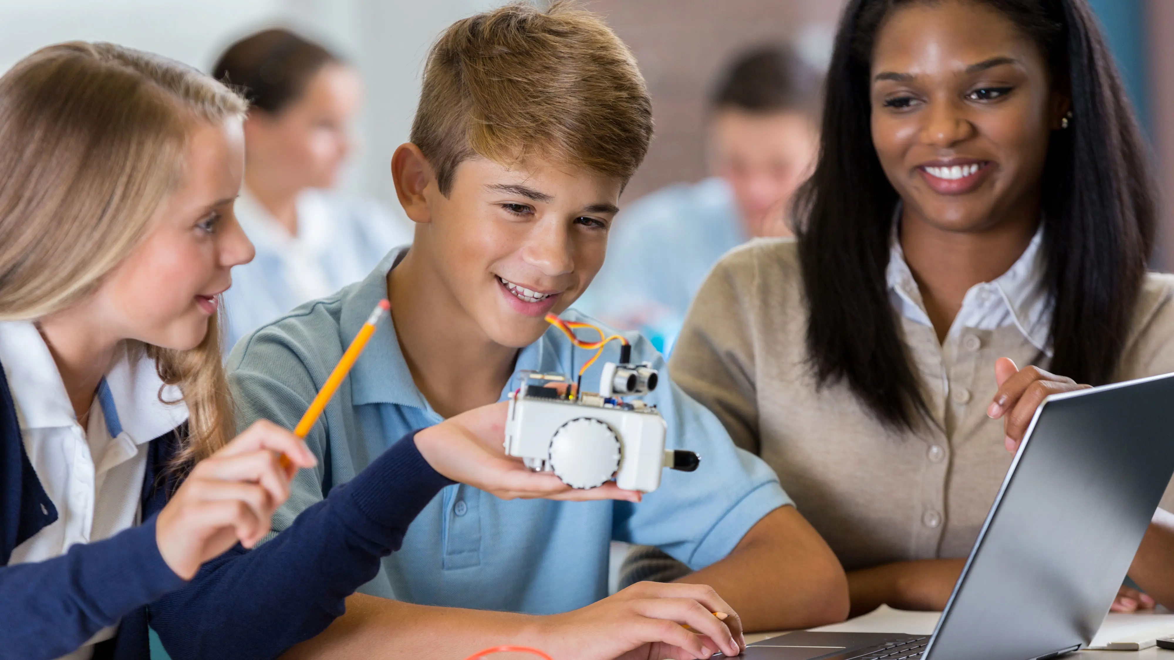 Two students working via a laptop on a eletrical device with a teacher supervising