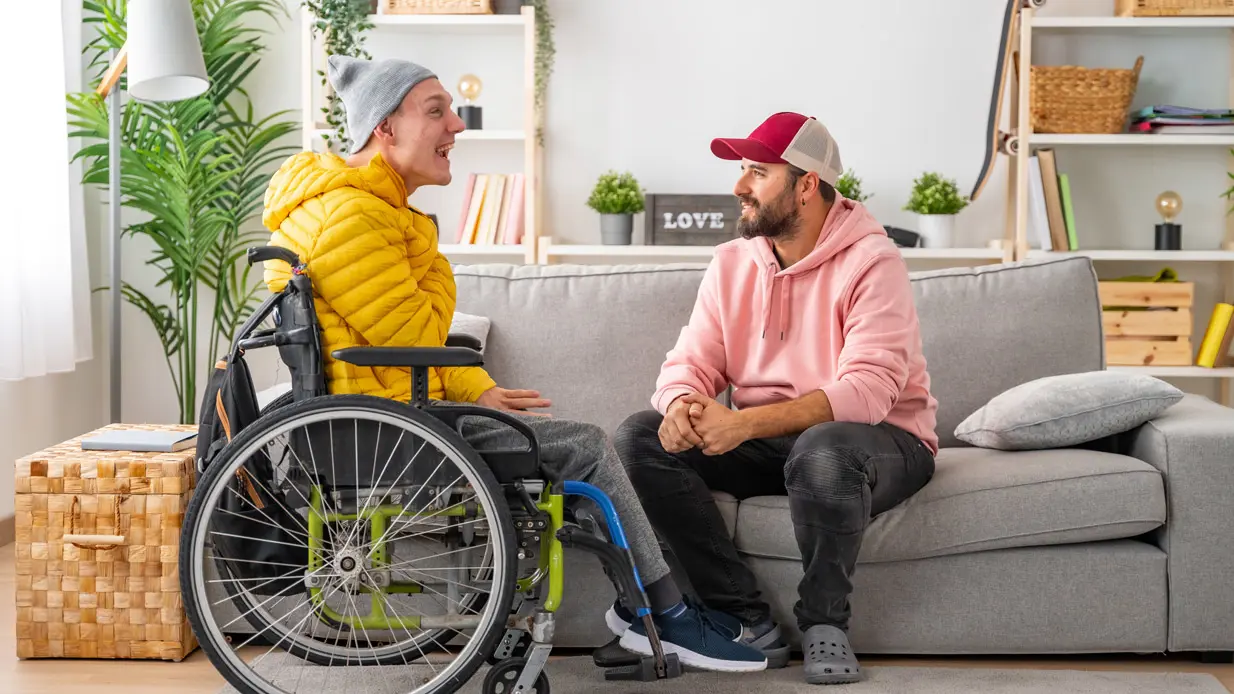 Two men in wheelchairs engaged in a conversation, sharing smiles and ideas in a friendly exchange.