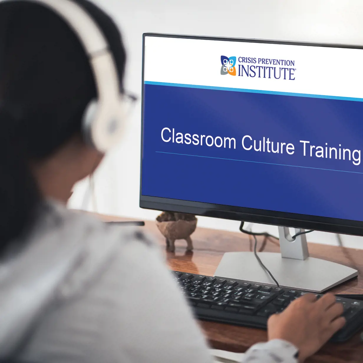 Woman with headphones watching Classroom Culture training on a laptop