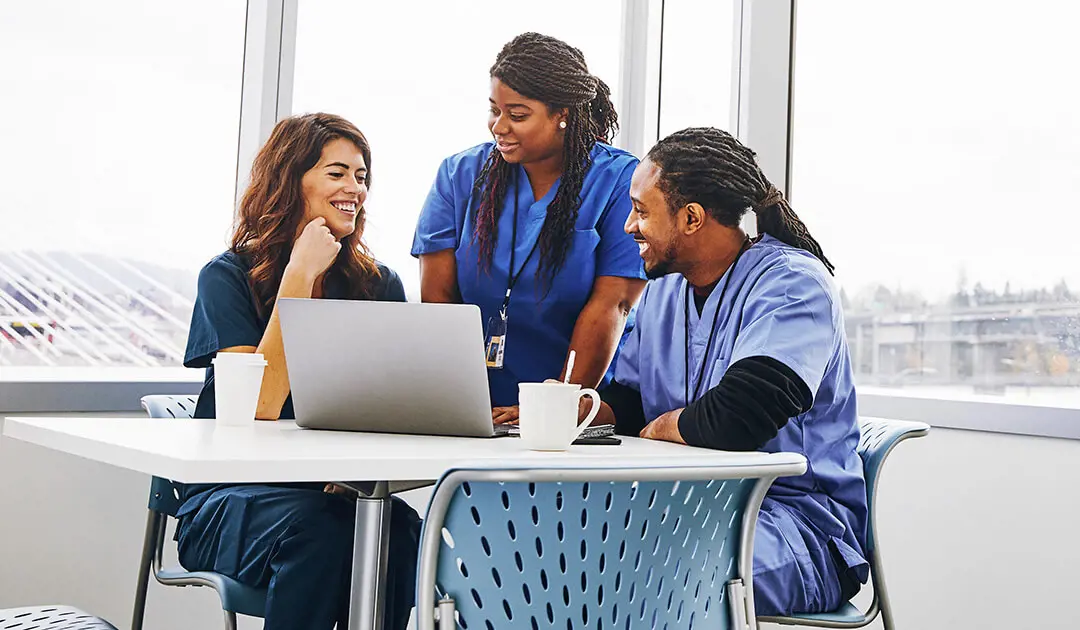 Three nurses talking around a laptop