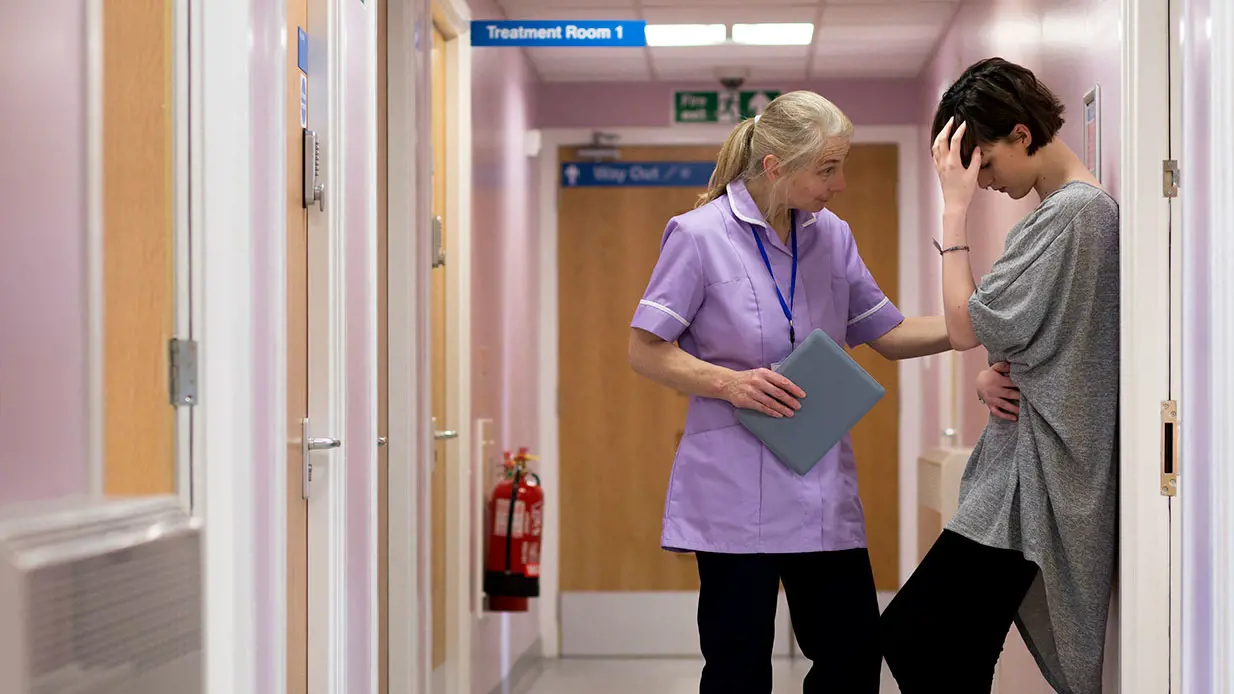 A female nurse consoling a patient in a hallway