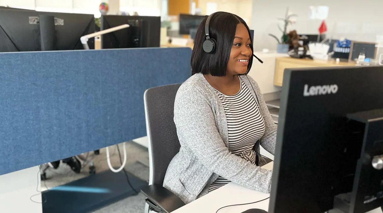 A smiling woman wearing a headset sitting at a computer. 