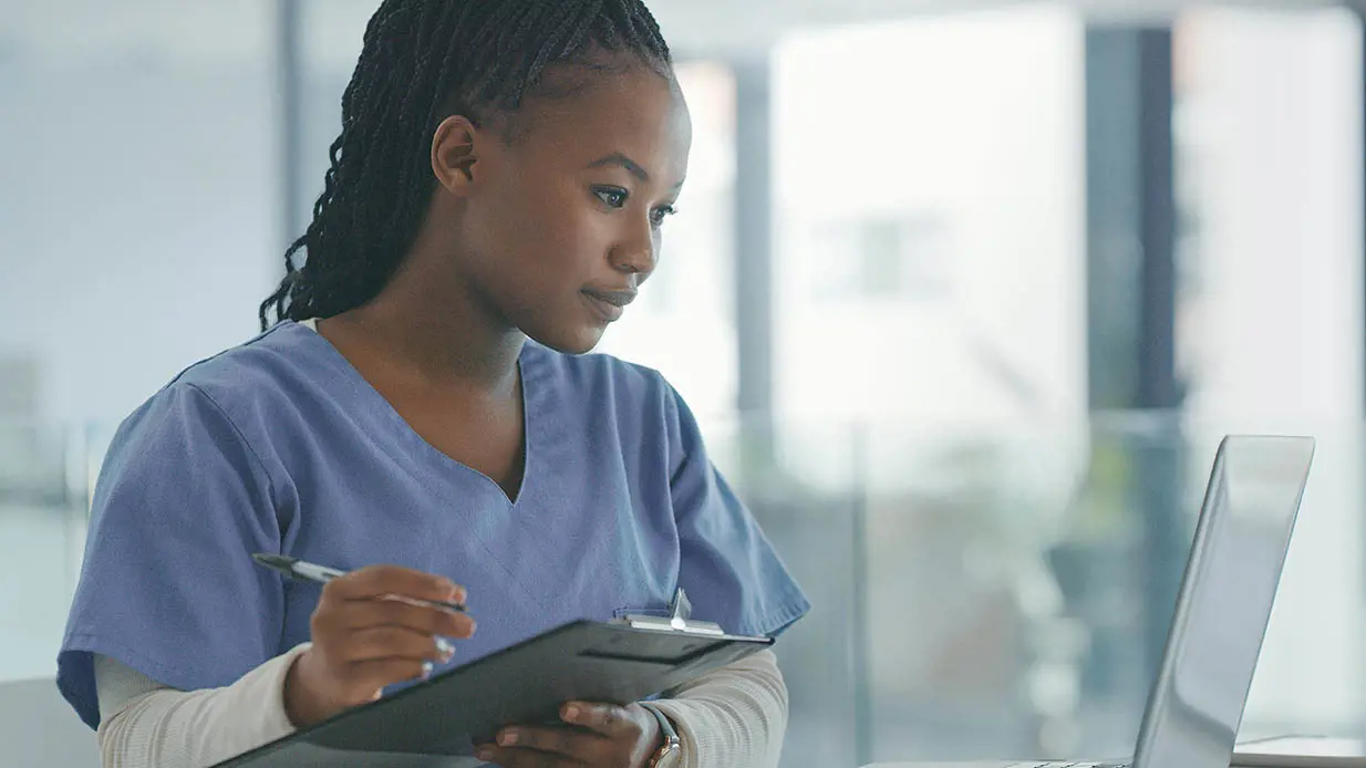 A medical professional taking notes as she looks at a computer screen. 
