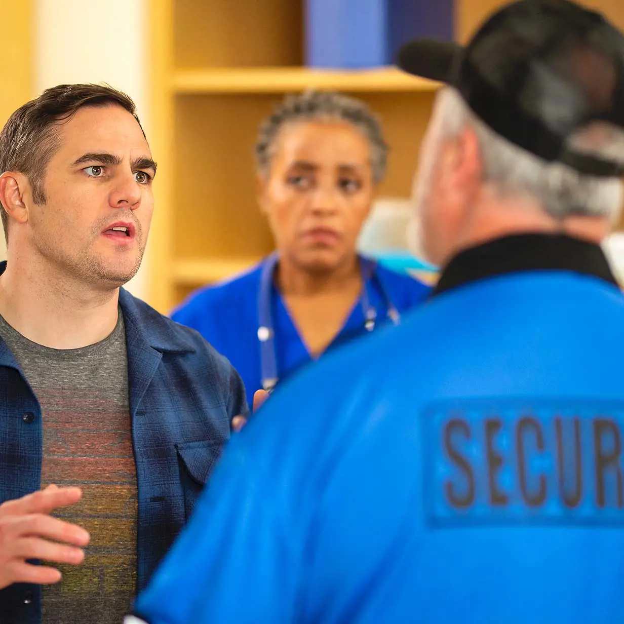 Security officer talking to an upset patient with a nurse in the background.