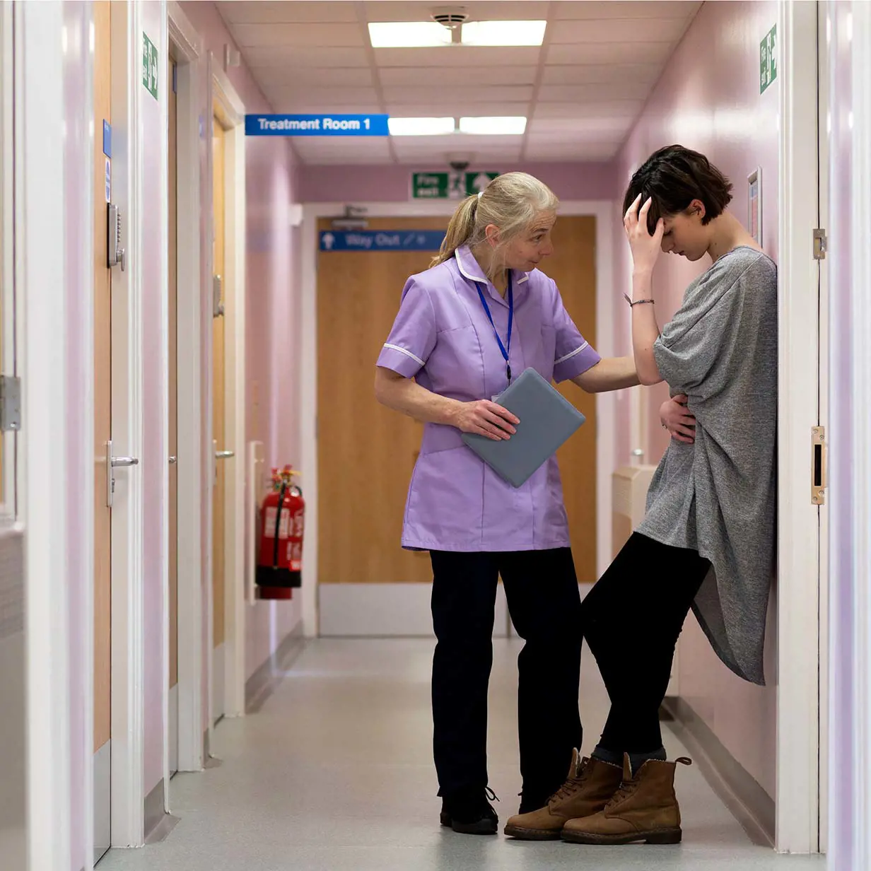 Female nurse talking to a sad patient in a clinic hallway.