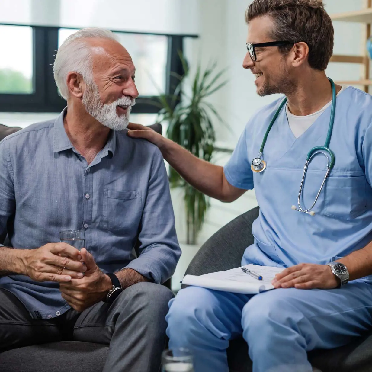 Male doctor talking with older male patient with his hand on his shoulder smiling.