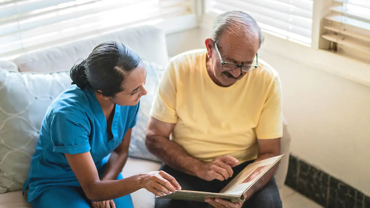 A medical professional reading a book with an elderly patient.