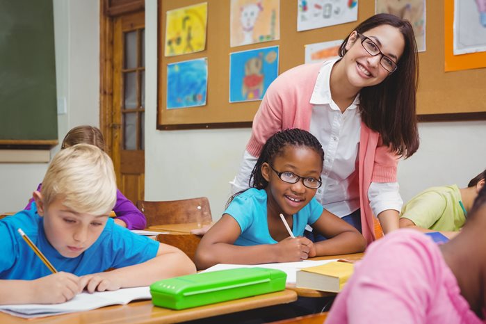 Teacher with glasses smiling while students work at desks